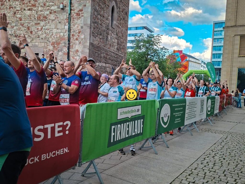 Läufer und KMS-Teammitglieder klatschen hinter Absperrgittern im Startbereich beim Firmenlauf Chemnitz